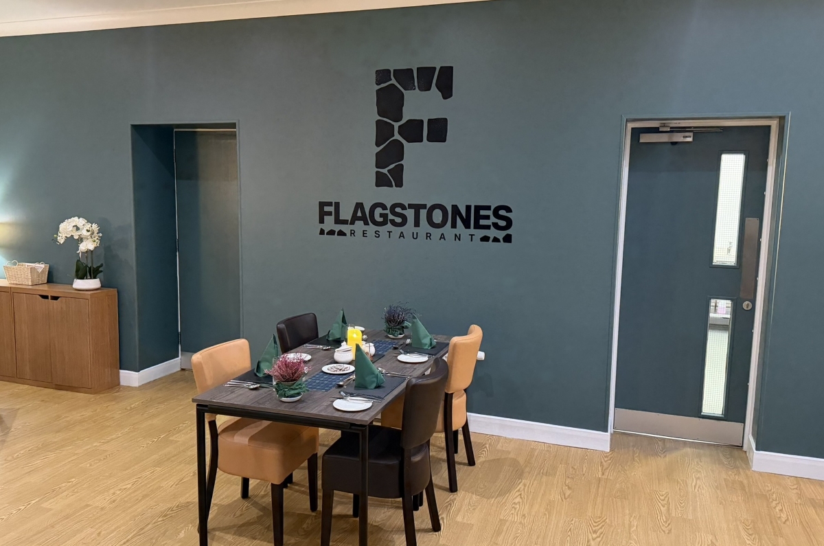 Photo of flagstones restaurant with dining table set for lunch, and Flagstones restaurant logo on the wall