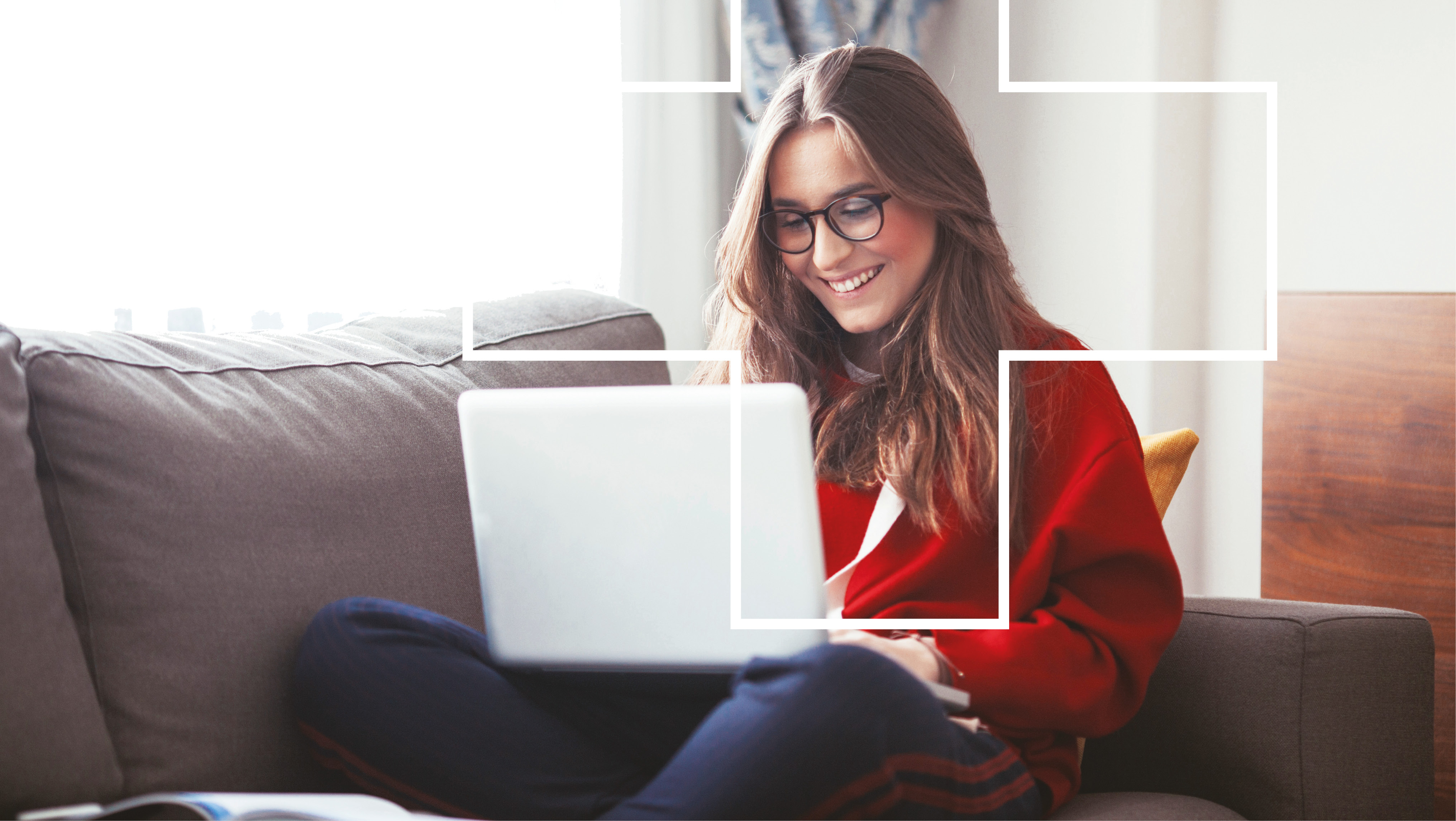 student learning remotely. Wearing glasses and red jumper, sitting on a sofa with a laptop