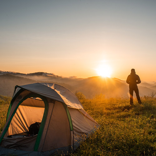 Scenic sunset view across Scottish mountains with a tent and an adventurer's silhouette