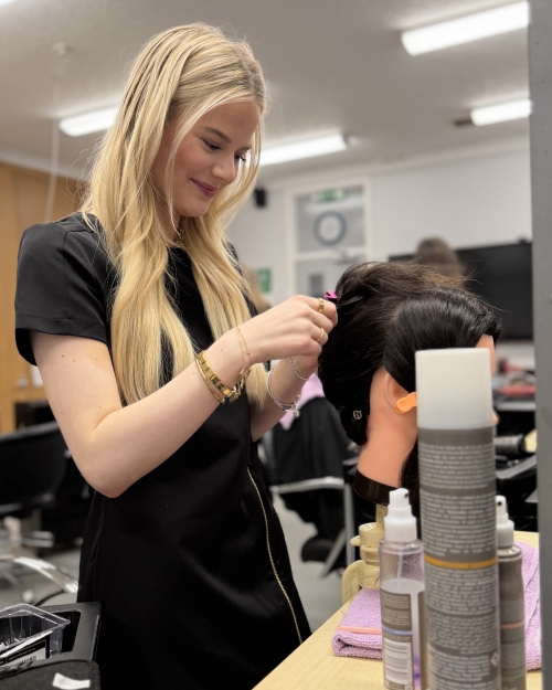 senior phase student Naomi Reid practising a hairstyle on a model head in the Thurso hairdressing salon