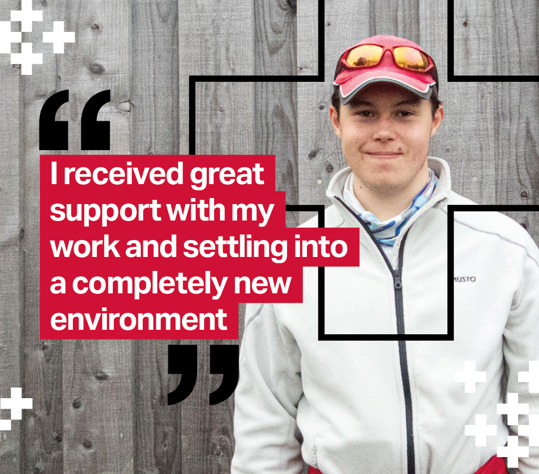 A smiling young man in a white fleece jacket and red cap stands against a wooden fence. Overlaid text on a red background reads: 