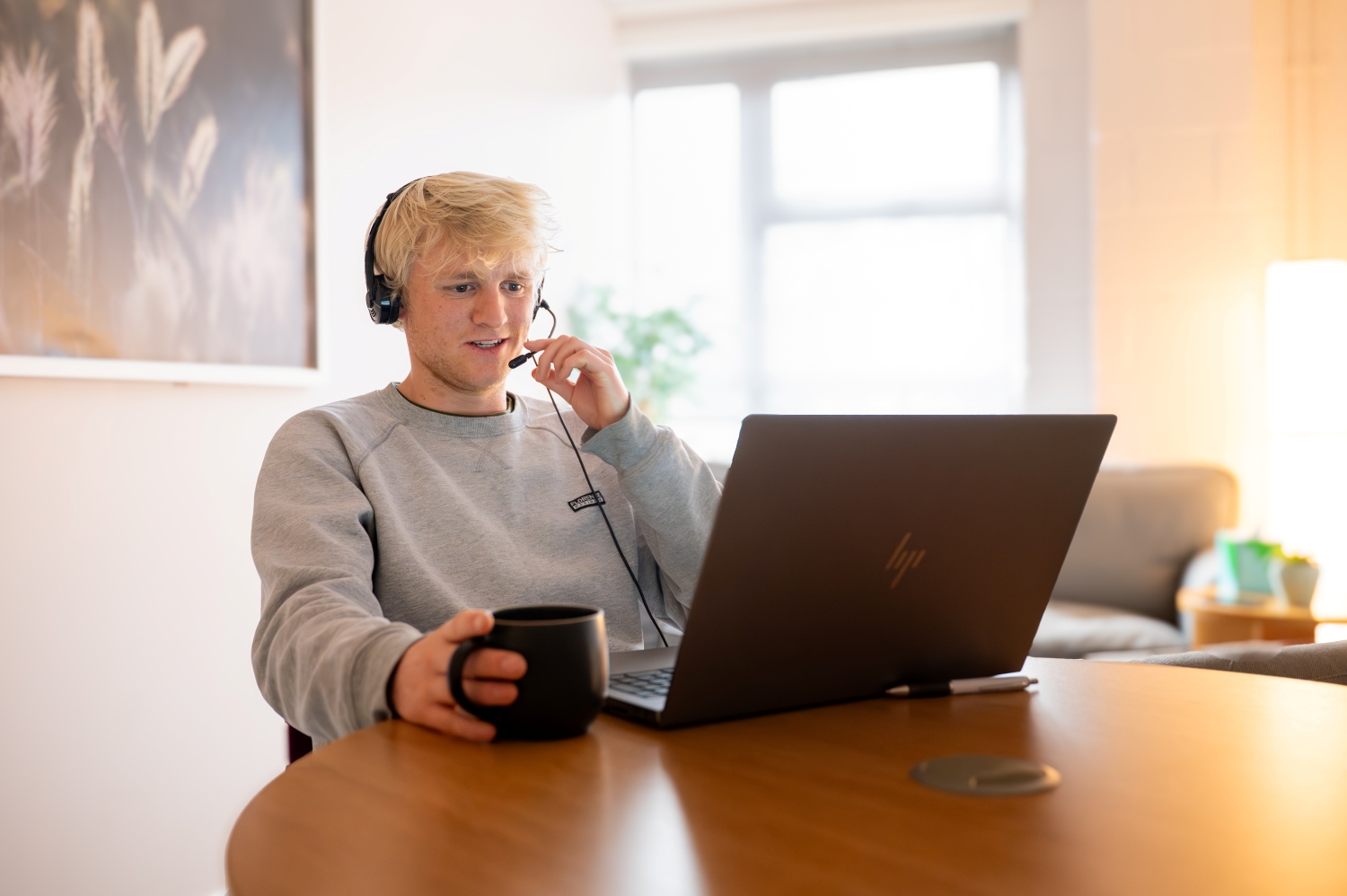 Student studying online from home, wearing a headset and using a laptop with a coffee mug in hand, in a bright, relaxed living space Student studying online from home, wearing a headset and using a laptop with a coffee mug in hand, in a bright, relaxed living space