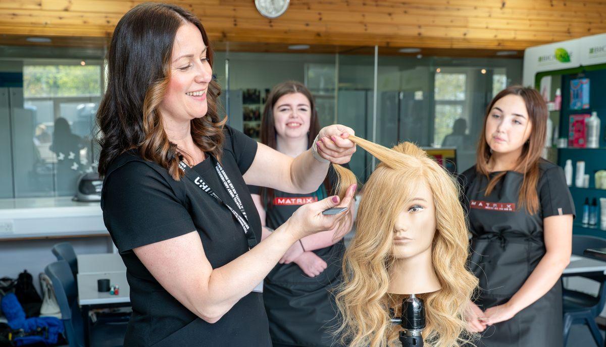 two students watching lecturer demonstrate hair style technique on model head in the salon in Stornoway