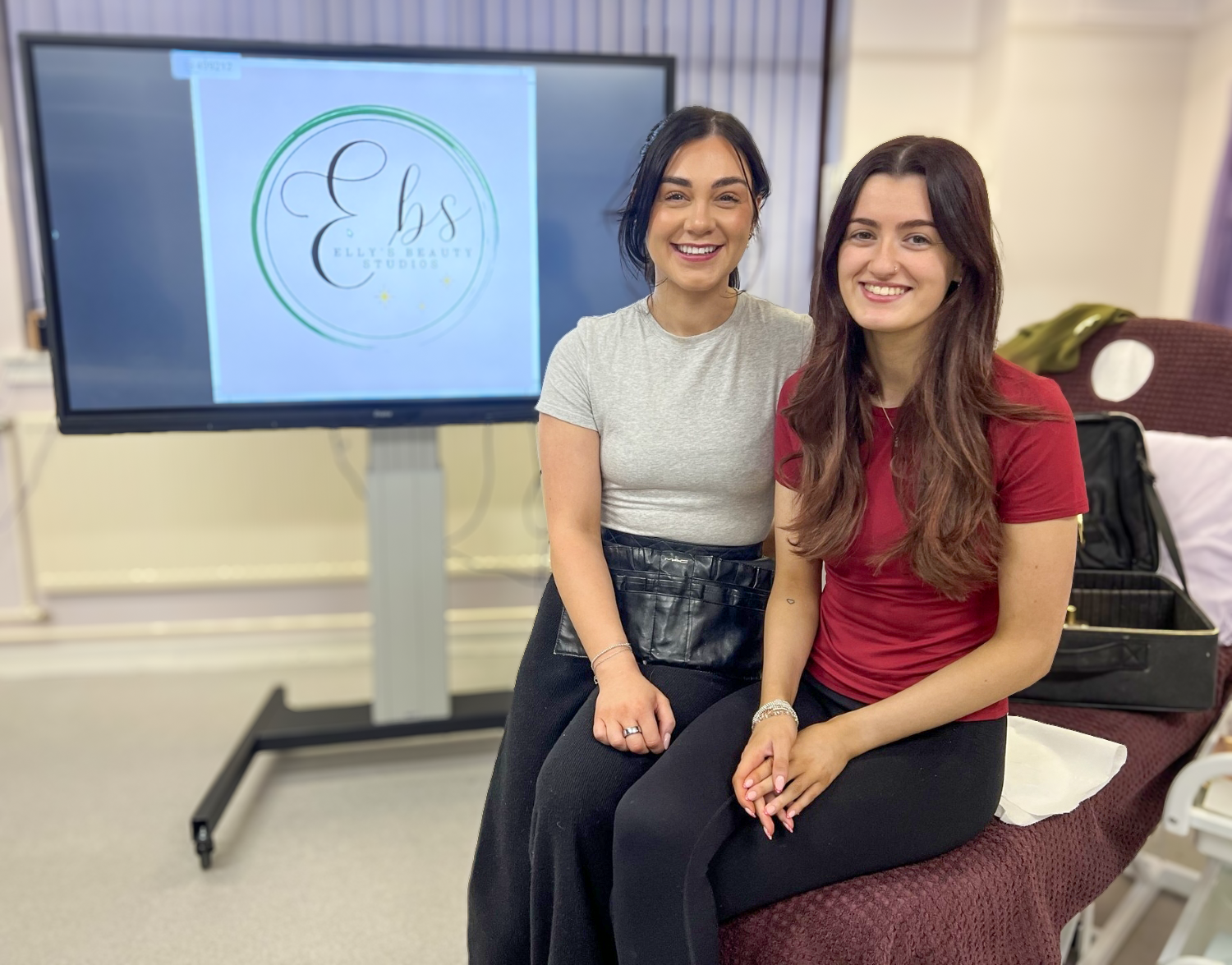 EBS logo with Elly Sutherland and Corina Swanson in the salon with makeup equipment