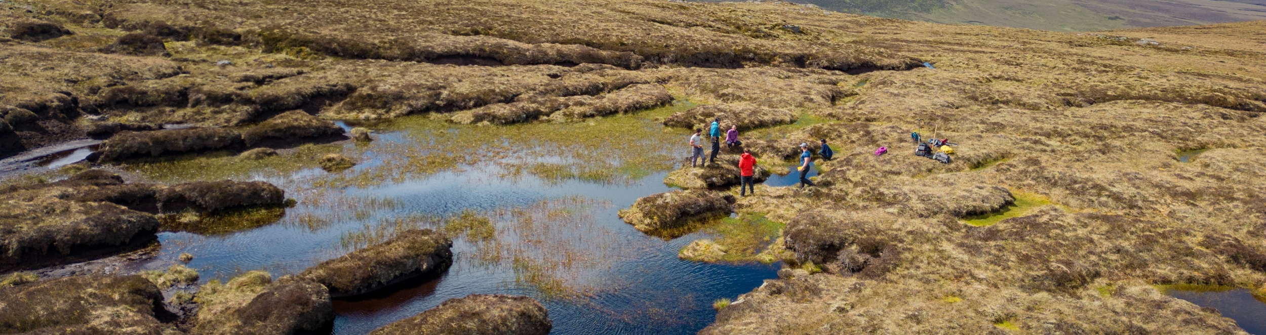 Group of people carrying out fieldwork among pools and exposed peat in a peatland landscape. Group of people carrying out fieldwork among pools and exposed peat in a peatland landscape.