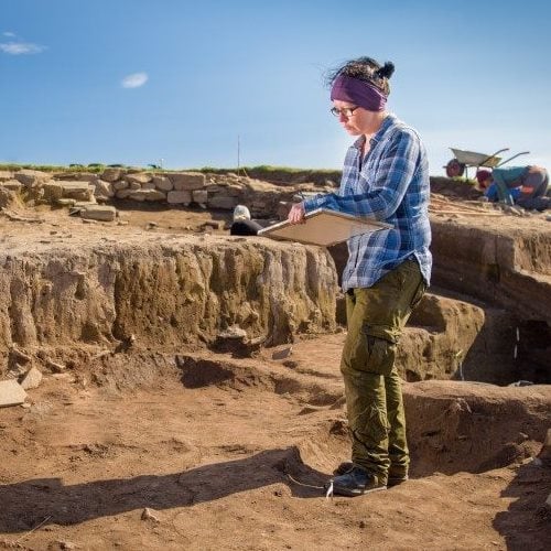 Mature female student studying board at an archaeological dig